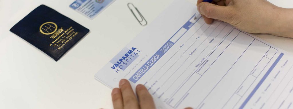 Mani che compilano una cartella clinica del Valparma Hospital accanto ad alcuni documenti personali