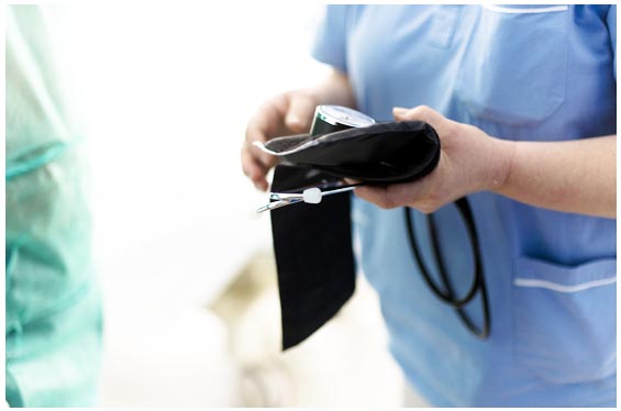 Operatore sanitario in divisa azzurra che tiene in mano un bracciale per misurare la pressione