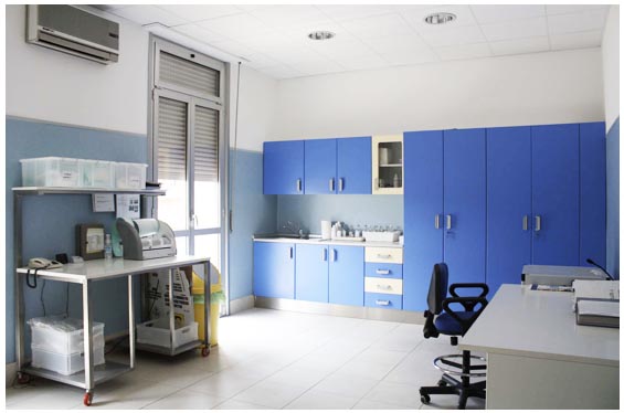 Ambulatorio con armadi blu, lavello, scrivania e carrello con materiale sanitario