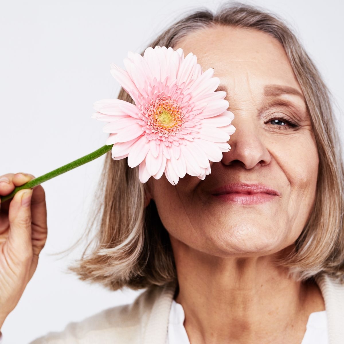 Donna matura sorridente che si copre un occhio con una gerbera rosa