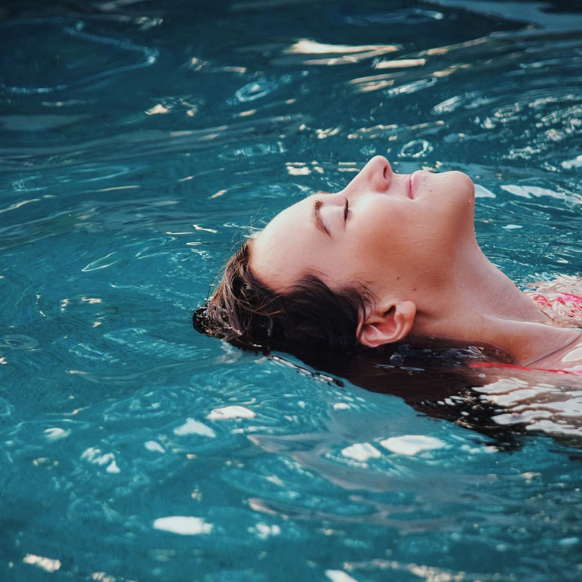 Donna che galleggia a occhi chiusi nell'acqua di una piscina