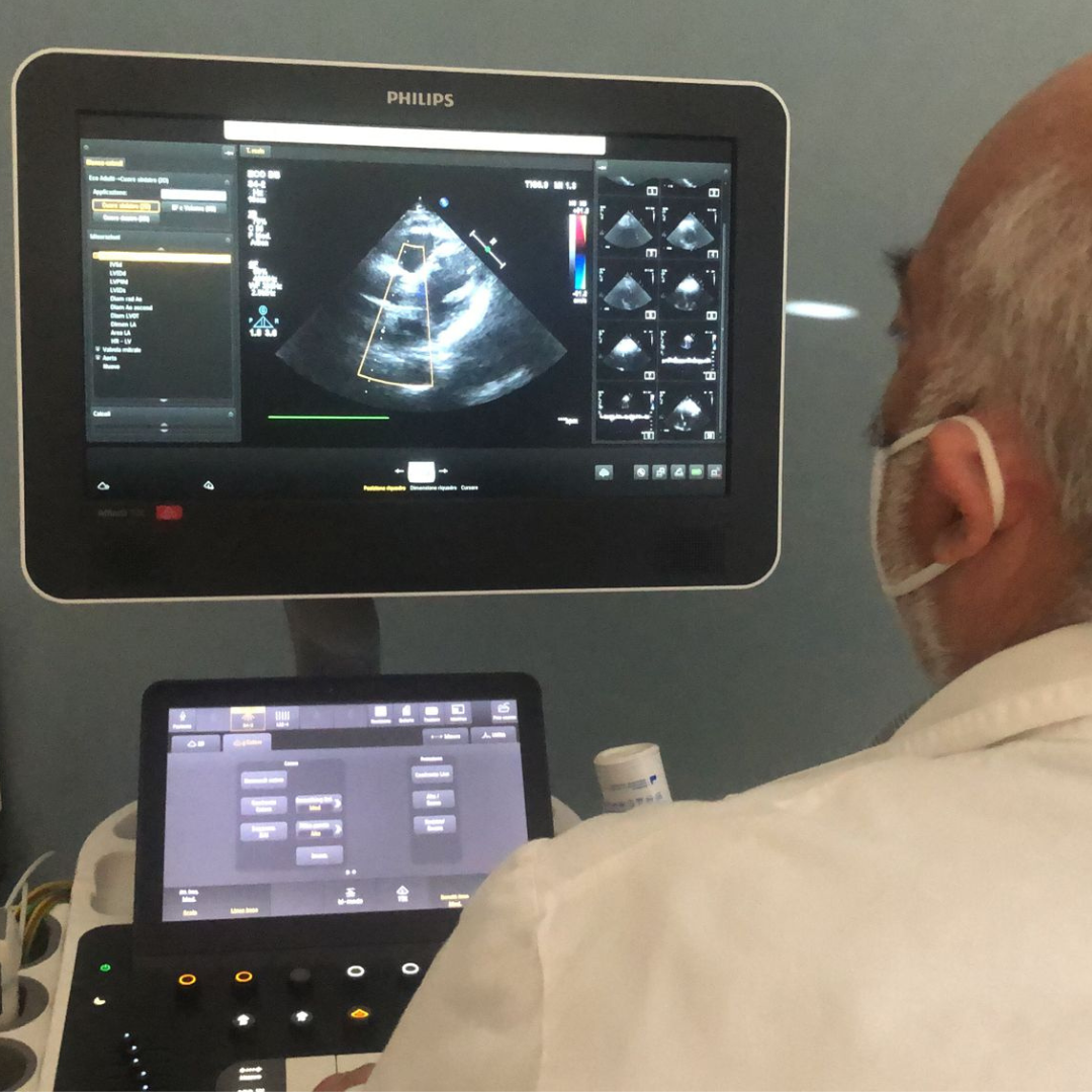 Medico con mascherina davanti a un ecografo che mostra le immagini di un'ecocardiografia