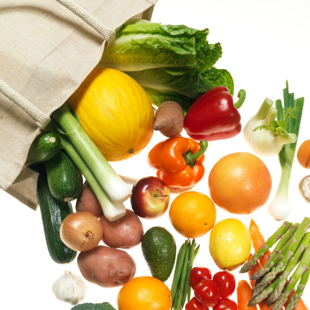 Borsa di tela da cui escono frutta e verdura: melone, peperoni, porri, arance, zucchine, patate e asparagi