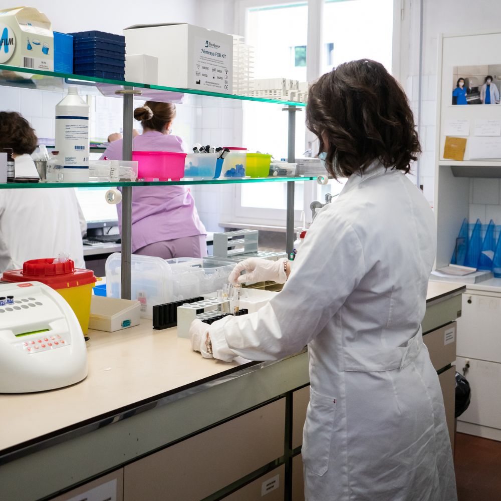 Operatrici in camice al lavoro sui banconi di un laboratorio di analisi, tra provette e strumenti