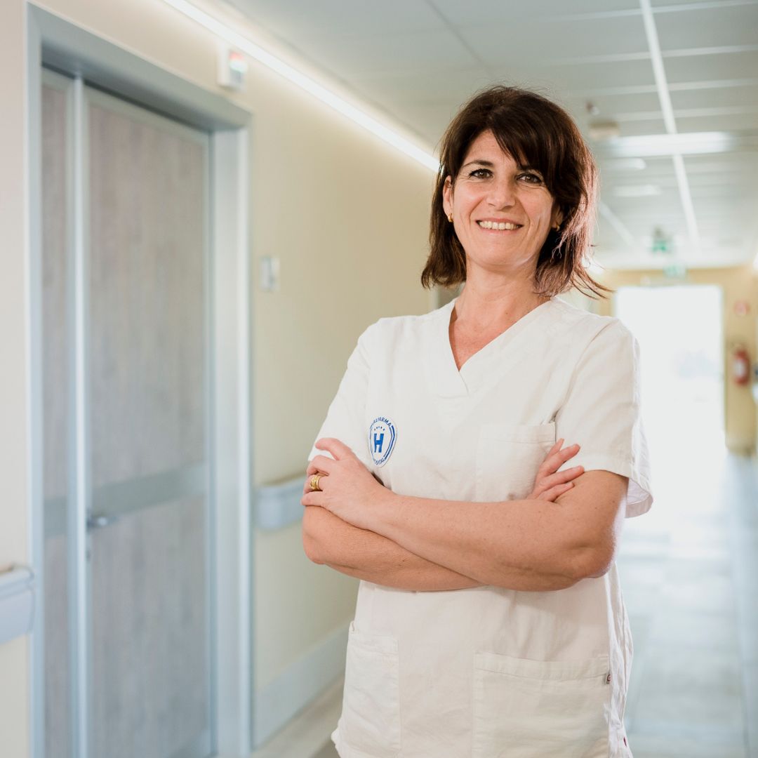 Operatrice sanitaria sorridente in divisa bianca, a braccia conserte in un corridoio di Valparma Hospital