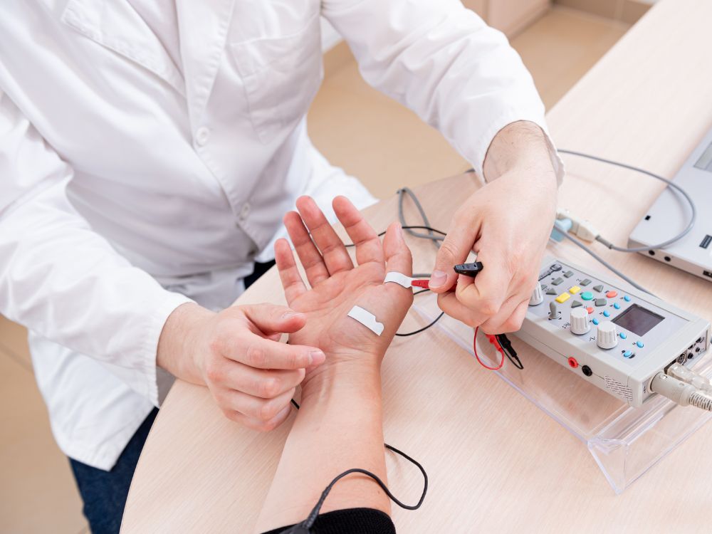 Medico che applica gli elettrodi sulla mano di un paziente per un'elettromiografia