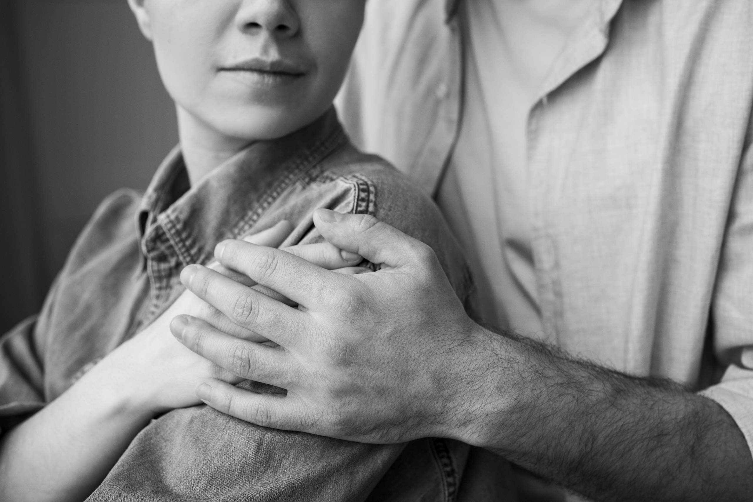 Uomo che stringe la mano di una donna appoggiata sulla sua spalla in un gesto di sostegno, in bianco e nero