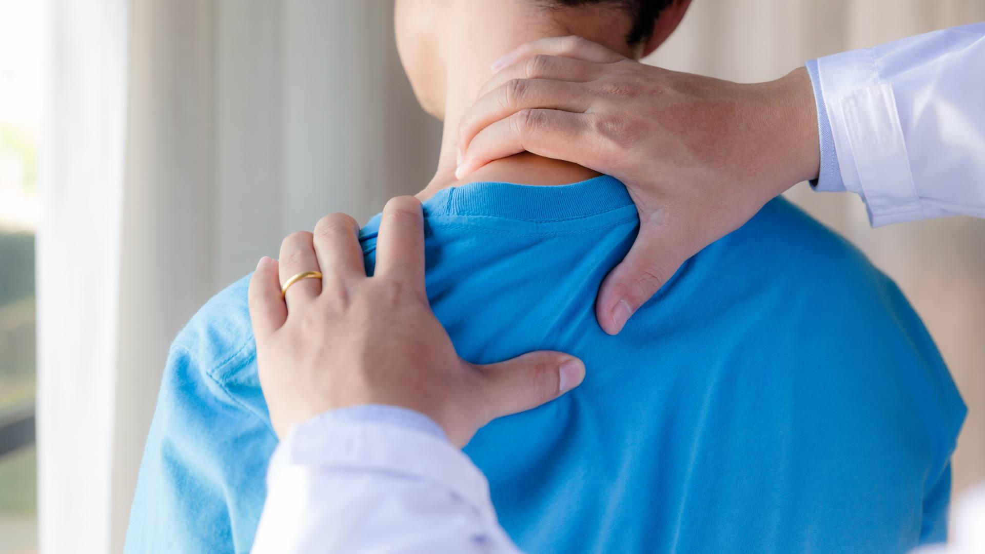Mani di un medico appoggiate sulla spalla e alla base del collo di un paziente con maglietta azzurra